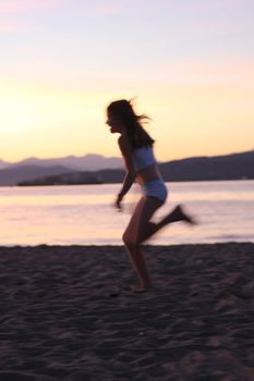Silhouette of a girl running along the beach at sunset, capturing motion and serenity.