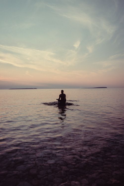 Free A person meditates in silhouette by the calm sea during sunset, creating a peaceful atmosphere. Stock Photo