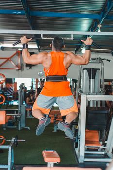 Muscular man in bright activewear doing pull ups in a gym setting.