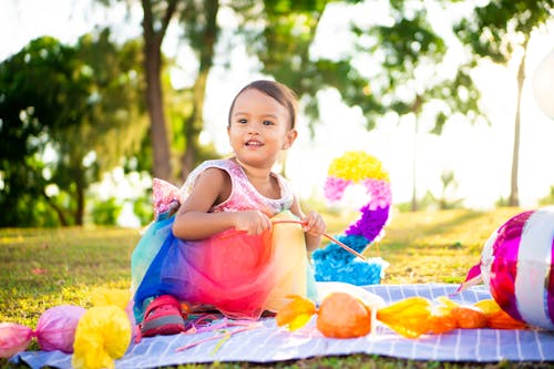 Shallow Focus of a Little Girl in Colorful Dress Sitting on Picnic Blanket