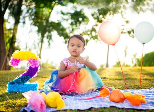 A Cute Baby Girl in Colorful Dress Sitting on a Picnic Blanket