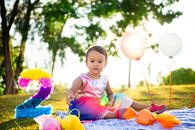 Girl in Pink Dress Sitting on Blue and Pink Textile Surrounded by Balloons