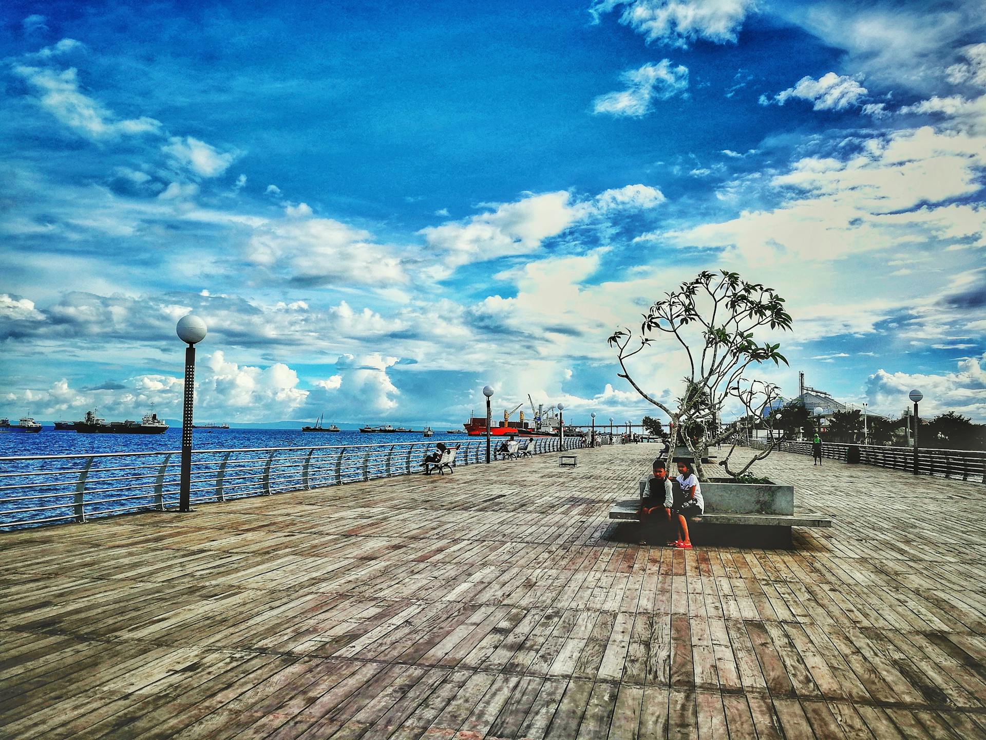 Relaxing view of a wooden boardwalk by the sea in Naga, Philippines, with ships on the horizon.