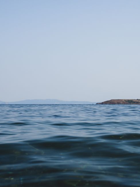 A serene view of the ocean with distant hills under a clear sky.