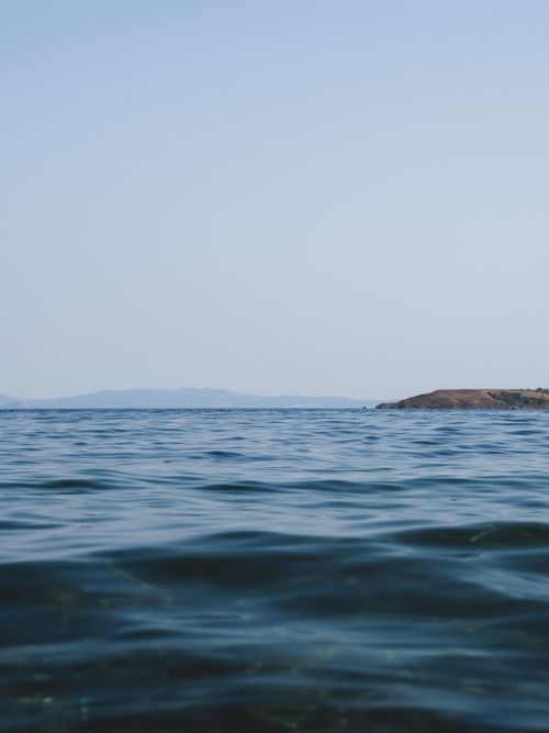 Free A serene view of the ocean with distant hills under a clear sky. Stock Photo