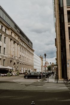 City street with parked cars and historical buildings under a cloudy sky.