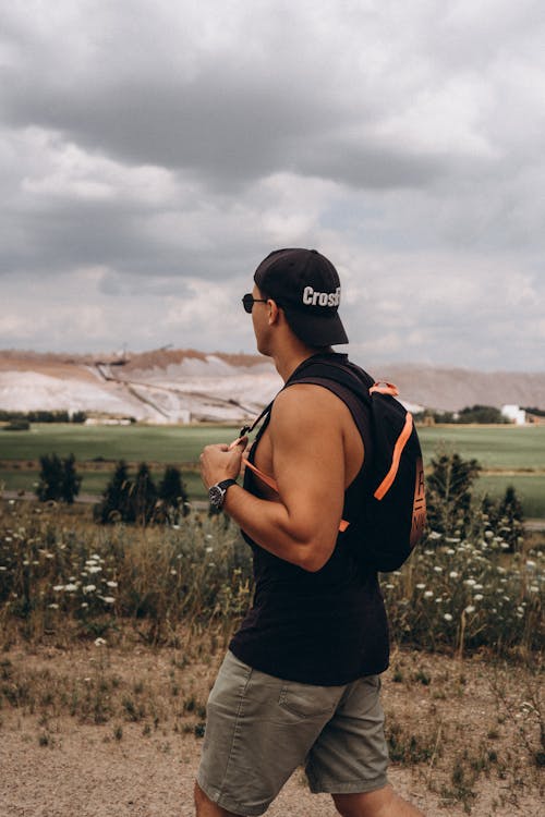 Man in Black Tank Top and Shorts Wearing Backpack and Cap Walking 