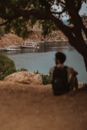 Man in Black Jacket Sitting on Brown Rock Near Body of Water