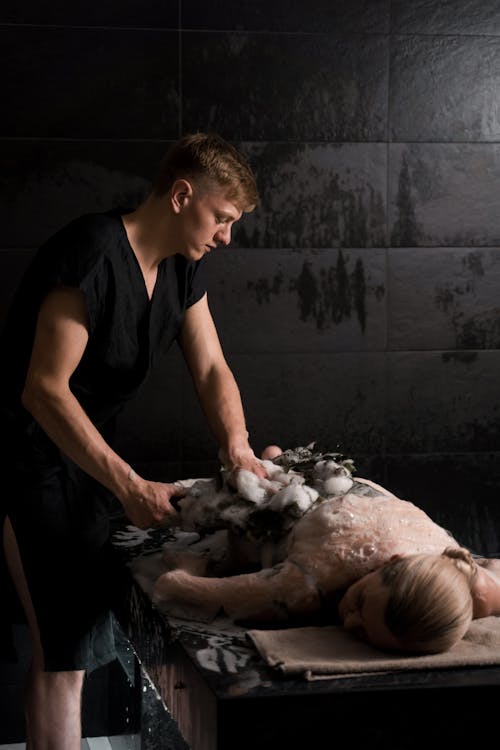 A Man in Black Robe Serving a Woman Client in a Spa Bathroom