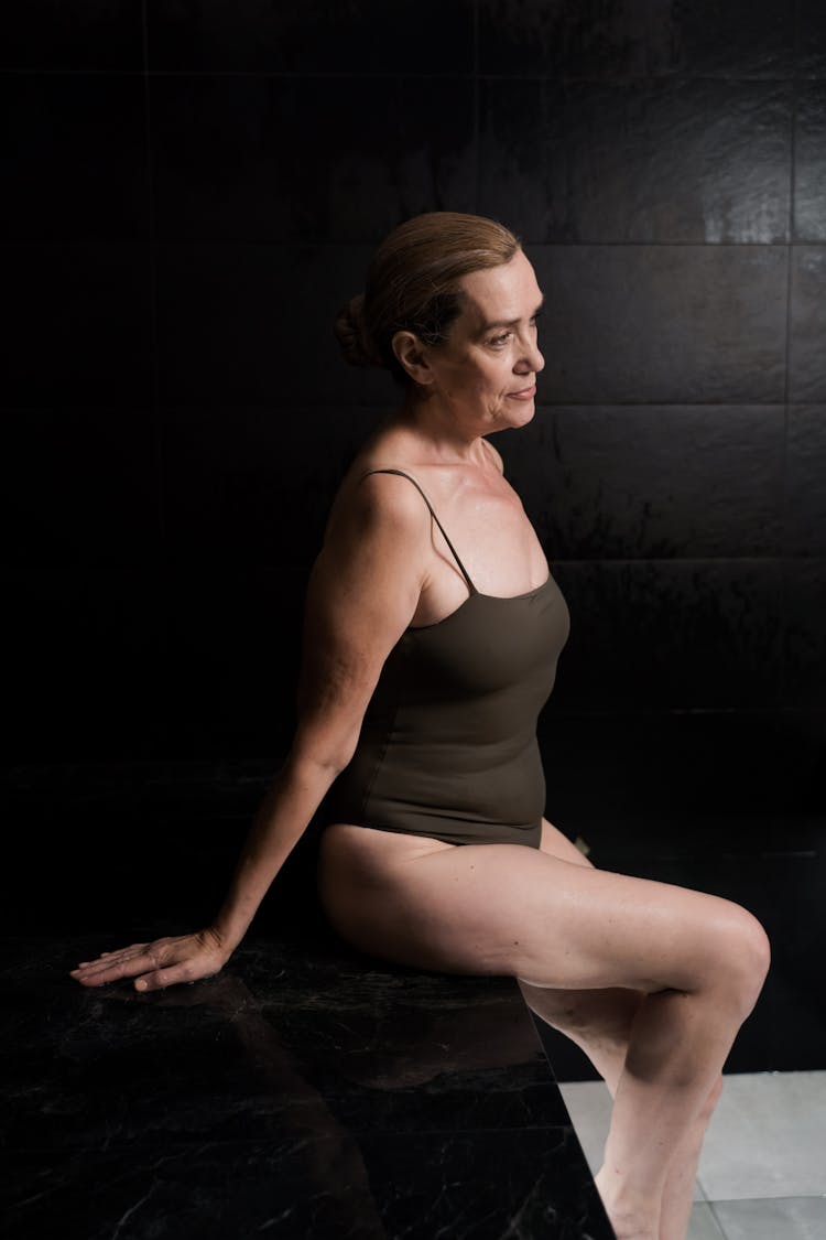 An Elderly Woman Wearing Swimsuit While Sitting On A Black Surface