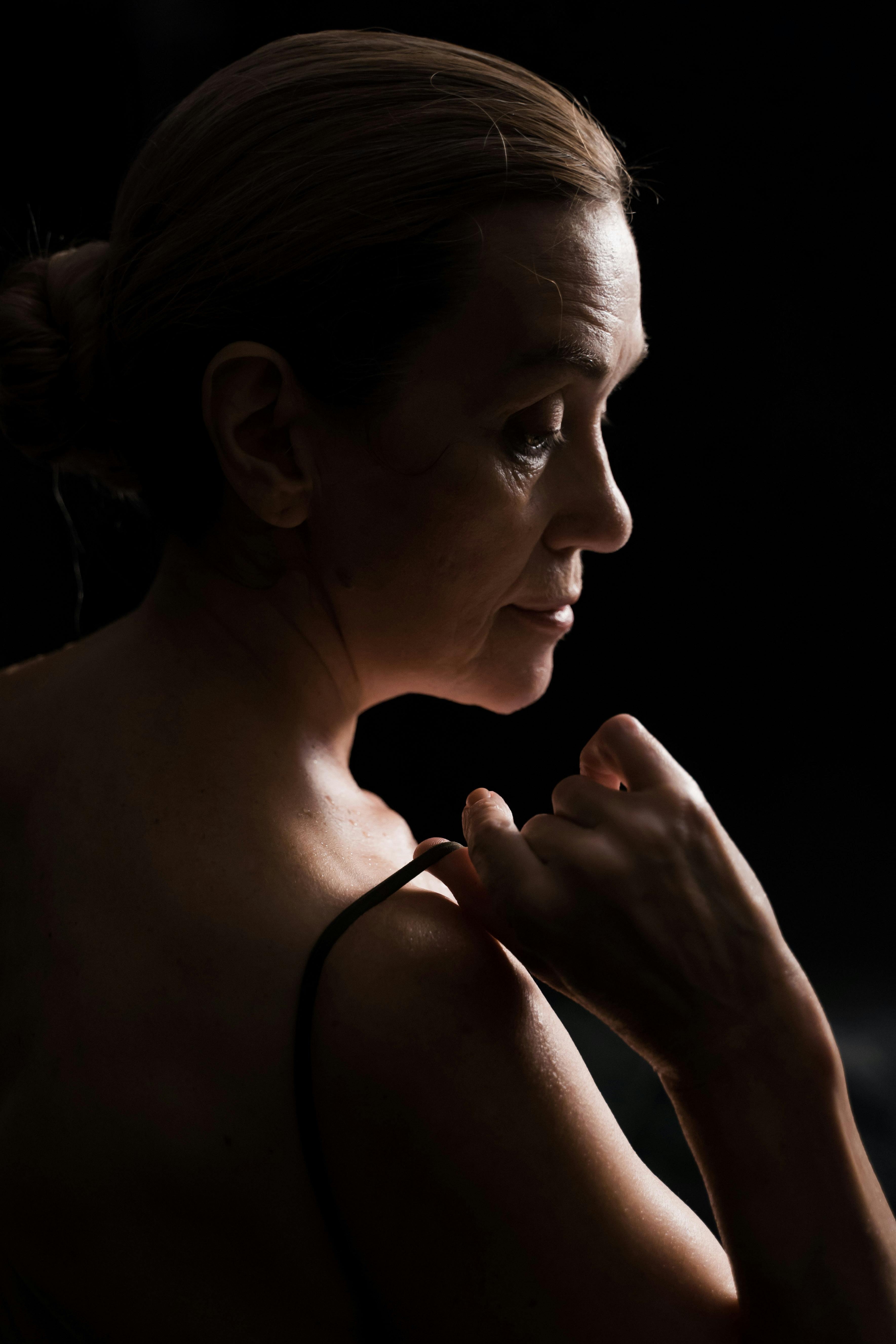 Profile of an elegant mature woman in dim lighting, creating a thoughtful ambiance.