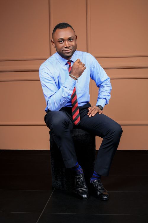 Free African man seated in formal wear, smiling in a professional setting. Stock Photo