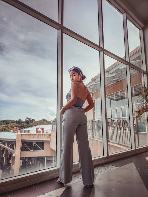 A Woman in Gray Pants Standing Near the Glass Windows while Looking Over Shoulder