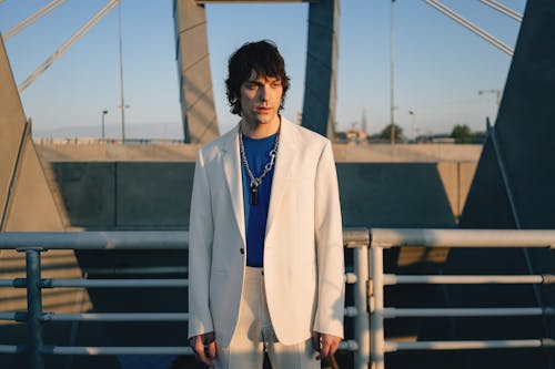 Man in a Blue Shirt and Beige Suit Leaning on Metal Railings