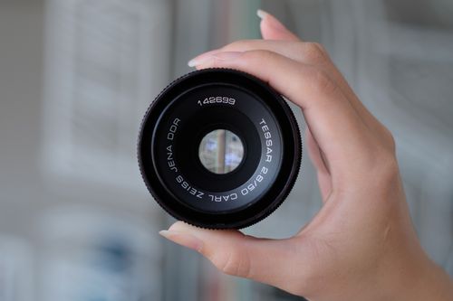 Free Close-up shot of a hand holding a Carl Zeiss camera lens with a blurred background. Stock Photo
