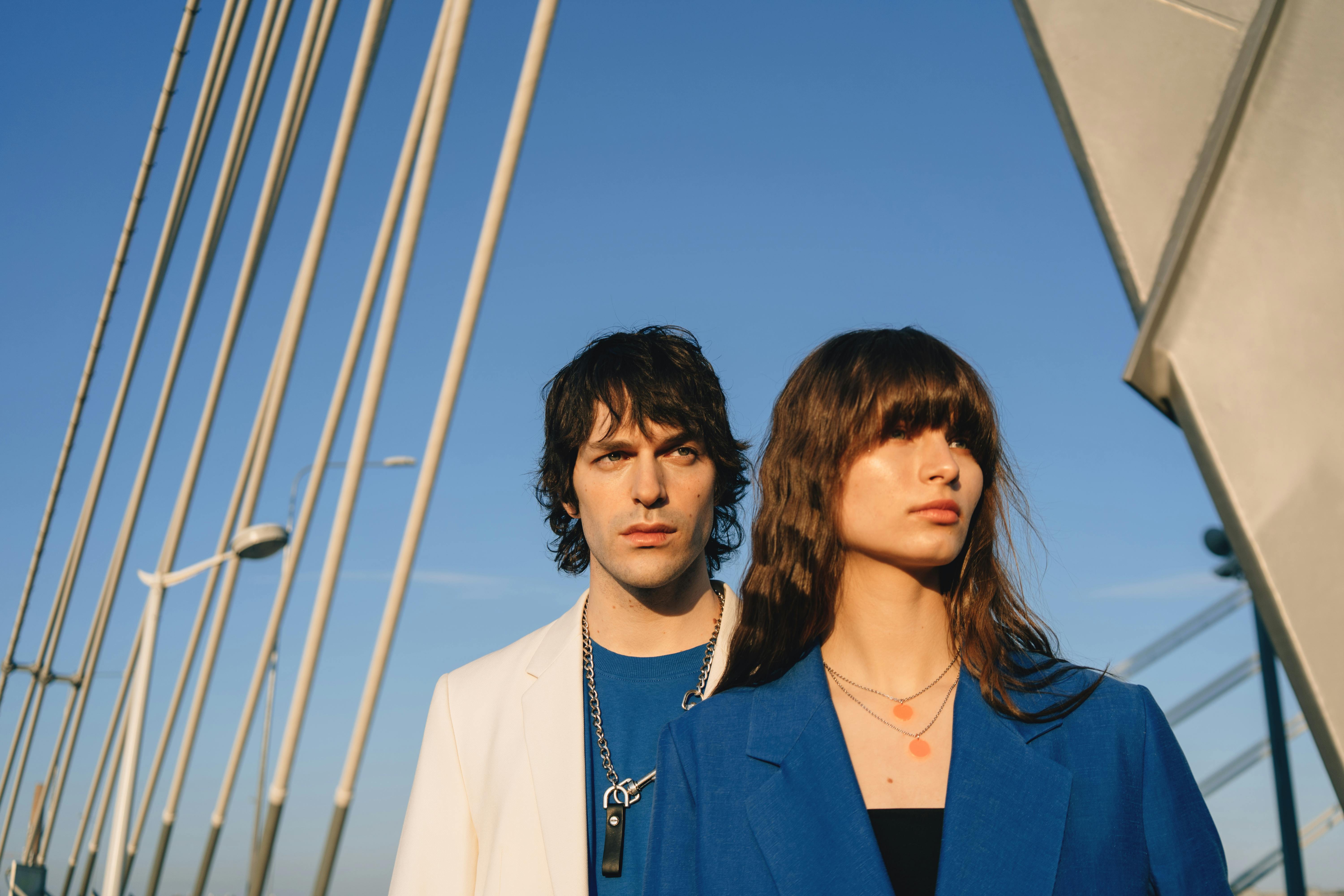Fashionable couple posing on a modern bridge beneath a clear blue sky, capturing urban style.