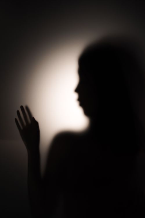 Free Artistic silhouette of a woman gesturing with hand against a softly lit wall. Stock Photo