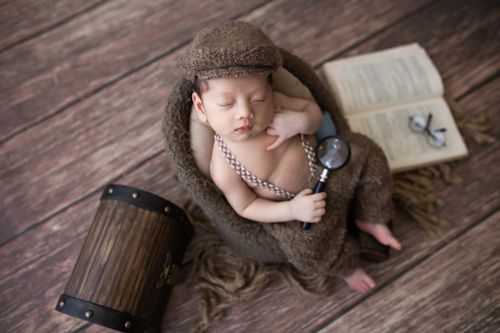 Free Adorable newborn dressed as a detective sleeping in rustic setting, holding magnifier. Stock Photo
