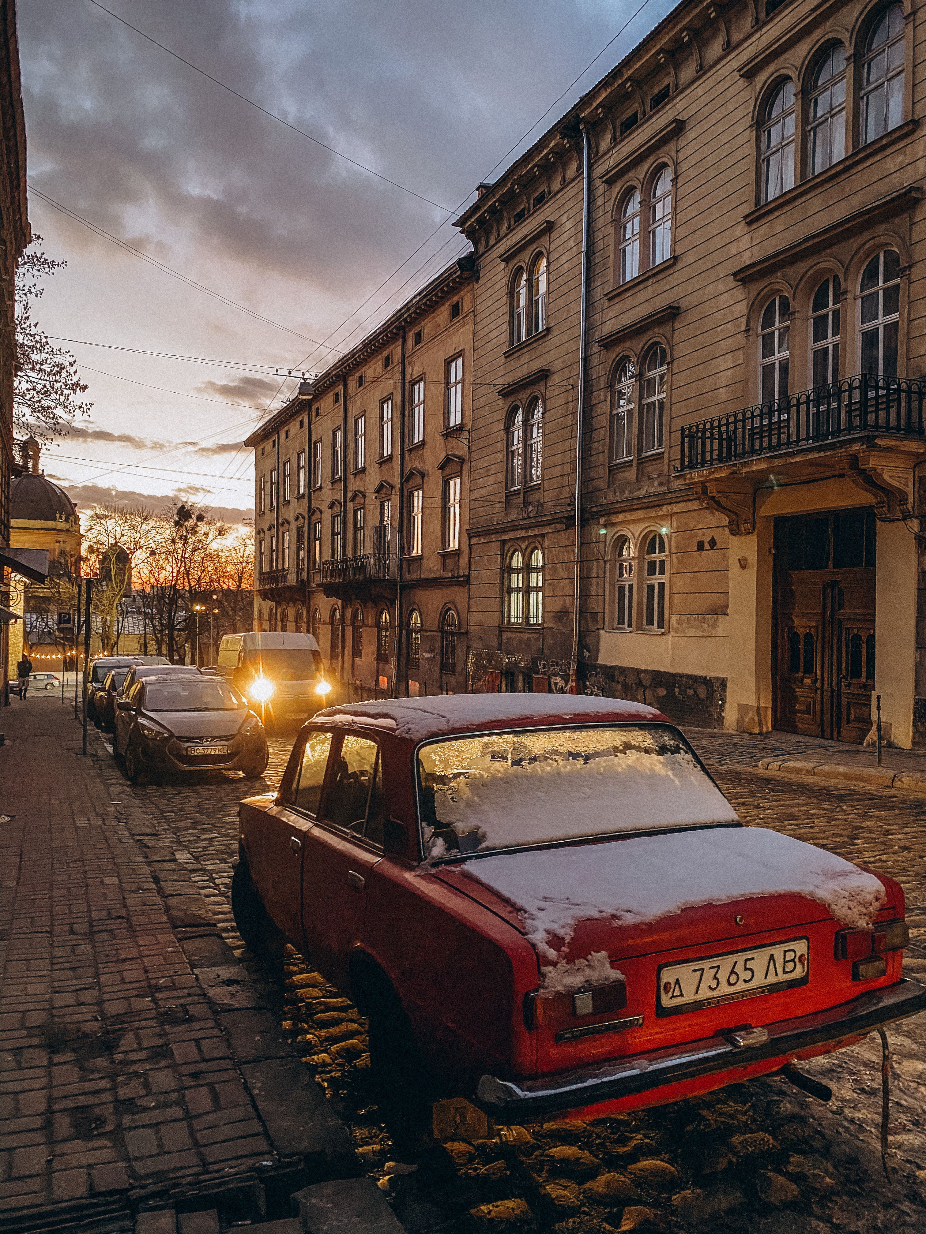 Cars on a Cobblestone Street between Buildings at Sunset · Free Stock Photo