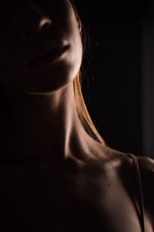Free Moody close-up of a woman's neck and shoulders in low light, highlighting skin texture and elegance. Stock Photo