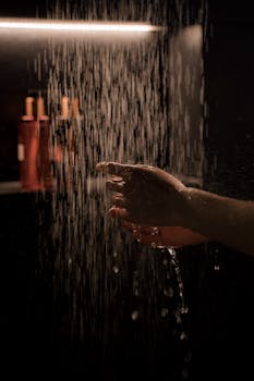 A tranquil hand under running water in a dimly lit shower setting, capturing moisture and ambiance.