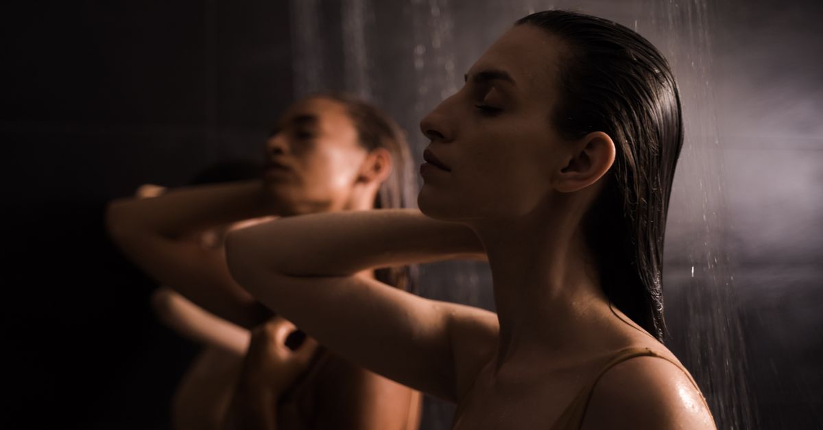 Person taking cold shower with steam rising, focused expression