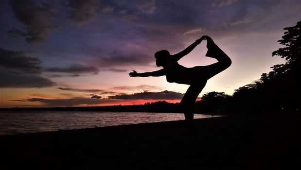 Silhouette of person doing yoga pose on beach at sunset in the Philippines.