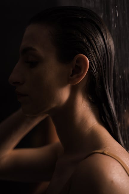 A serene side profile of a woman in the shower captured in warm lighting.