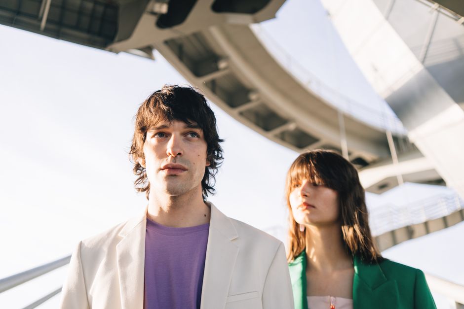 Stylish young couple in jackets standing beneath a modern architectural structure.