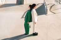 Woman in Green Coat and White Pants Walking on White Floor