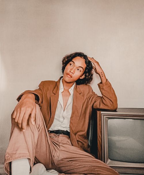 Free A stylish adult in brown attire thoughtfully poses indoors by a vintage television. Stock Photo