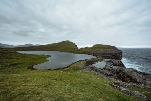 A Green Grass Field Near the Body of Water Under the Cloudy Sky