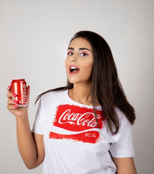 Free Portrait of a young woman holding a Coca-Cola can, expressing excitement against a white background. Stock Photo
