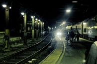 Dramatic night view of a train station with tracks and passengers under glowing lights.
