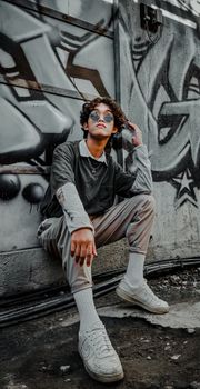 Stylish young adult posing against graffiti wall, showcasing contemporary street fashion in an urban setting.