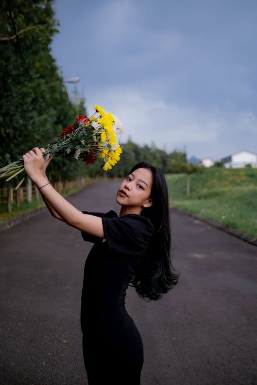 A Woman in Black Dress Holding a Bouquet of Flowers