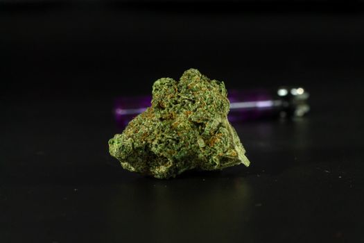 Detailed macro shot of a cannabis bud with a pipe in the background.