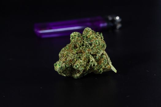 Macro shot of cannabis bud on black background with a purple lighter in the background.
