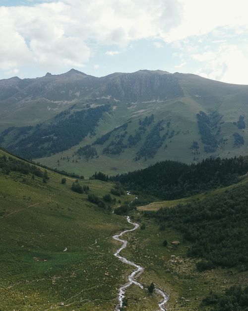Free Explore a tranquil valley with a meandering river set against majestic mountains under a bright sky. Stock Photo
