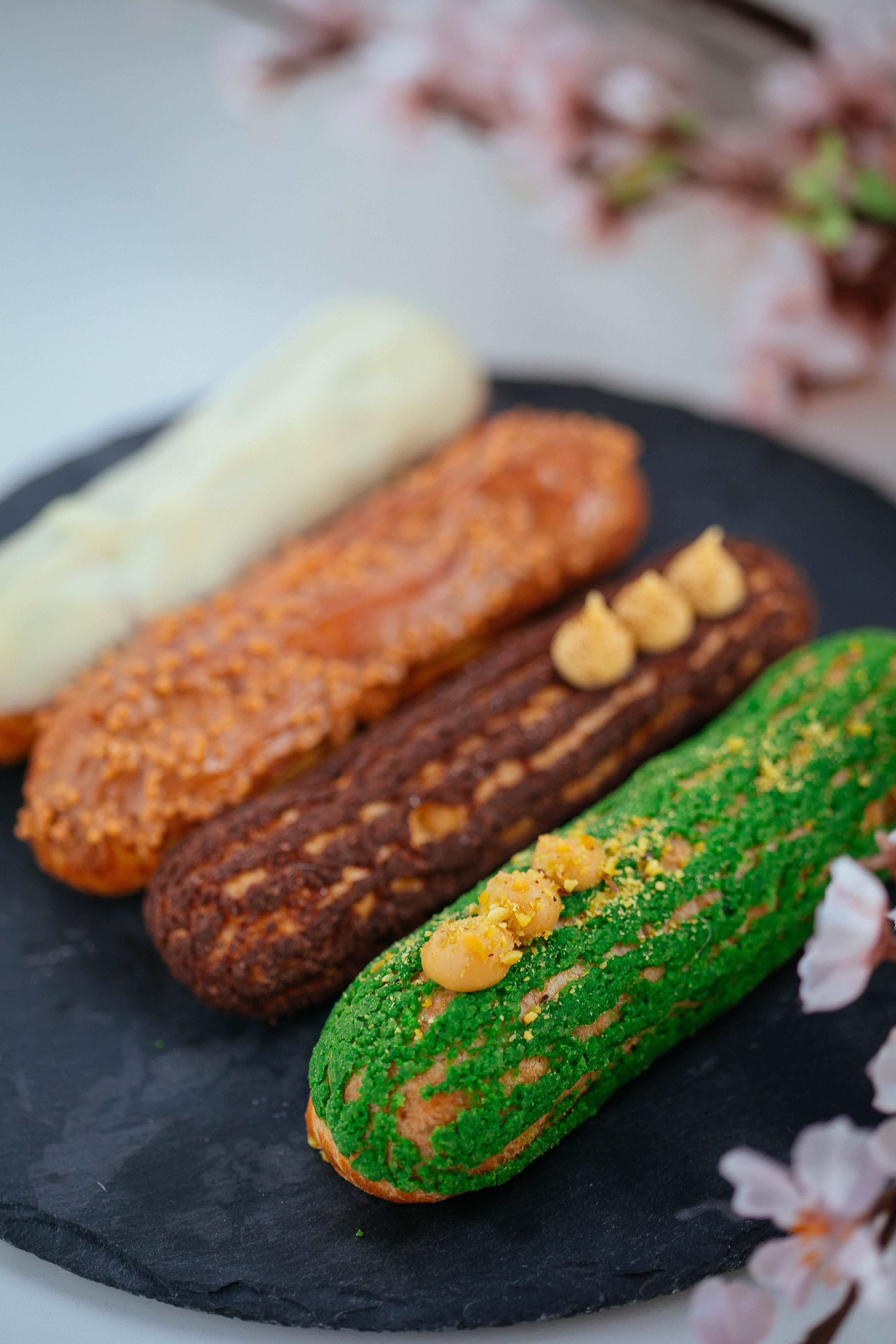 Four assorted eclairs on a slate plate surrounded by delicate flowers.