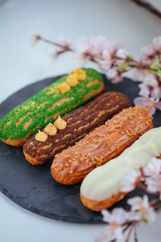 A visually appealing collection of four gourmet eclairs displayed on a slate plate surrounded by soft floral accents.