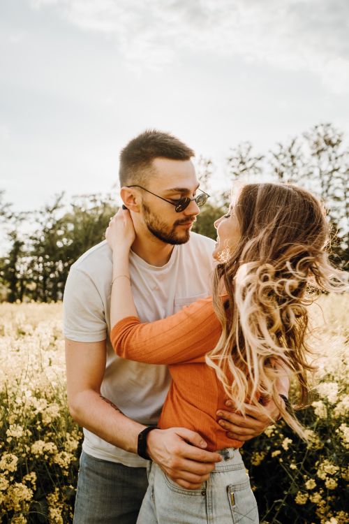 Free A couple shares a loving embrace in a sunny meadow, surrounded by flowers and nature. Stock Photo