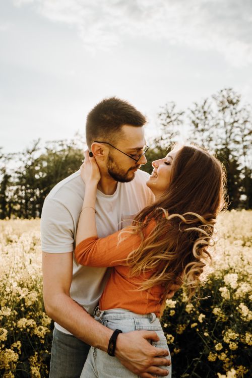 Free Joyful couple embracing in a vibrant flower field, showcasing love and romance outdoors under a sunny sky. Stock Photo