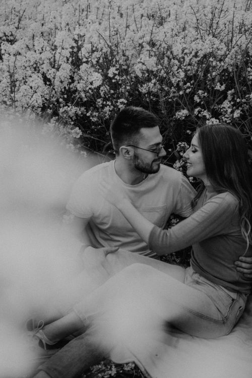 Free A couple sitting and embracing in a flower field, captured in soft grayscale tones. Stock Photo