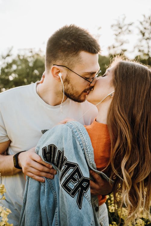 Free A young couple sharing a romantic kiss outdoors while listening to music with earphones. Stock Photo