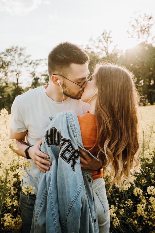 Free A couple shares a romantic kiss in a bright, sunlit field, wearing casual clothing. Stock Photo
