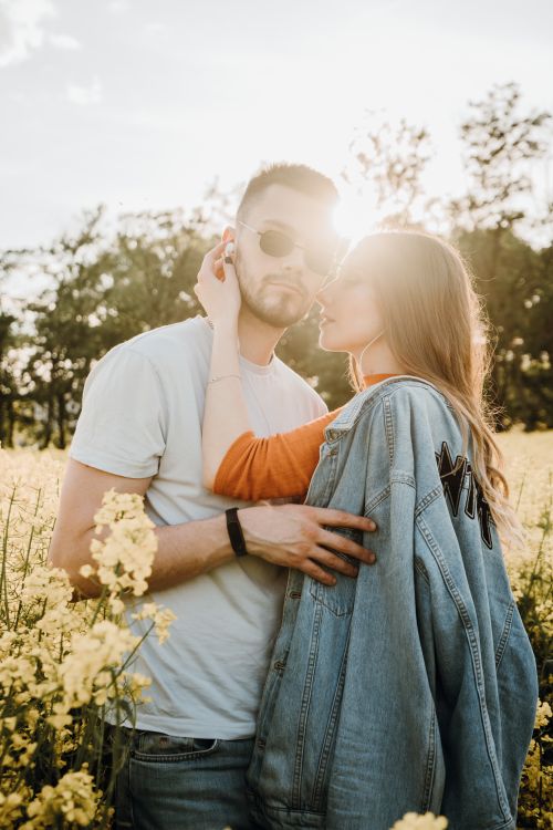 Free Young couple embracing in a sunlit field with yellow flowers, enjoying a romantic moment outdoors. Stock Photo