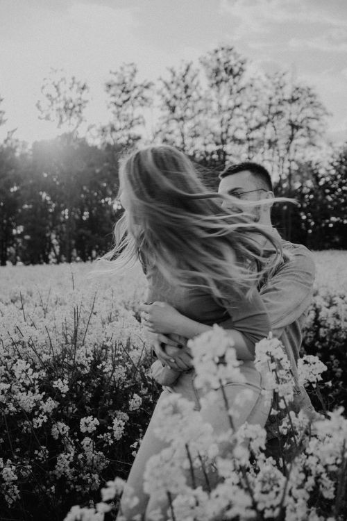 Free A romantic couple embracing in a blooming flower field, captured in monochrome. Stock Photo