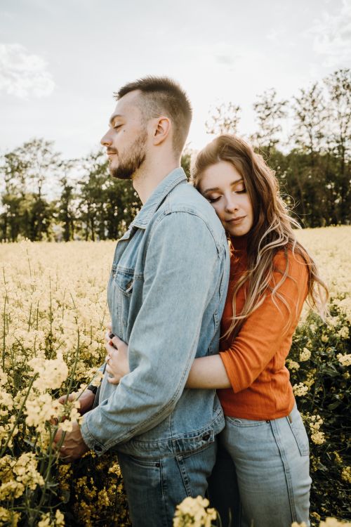 Free Couple embraces warmly in a sunny flower field, evoking romance and tranquility. Stock Photo
