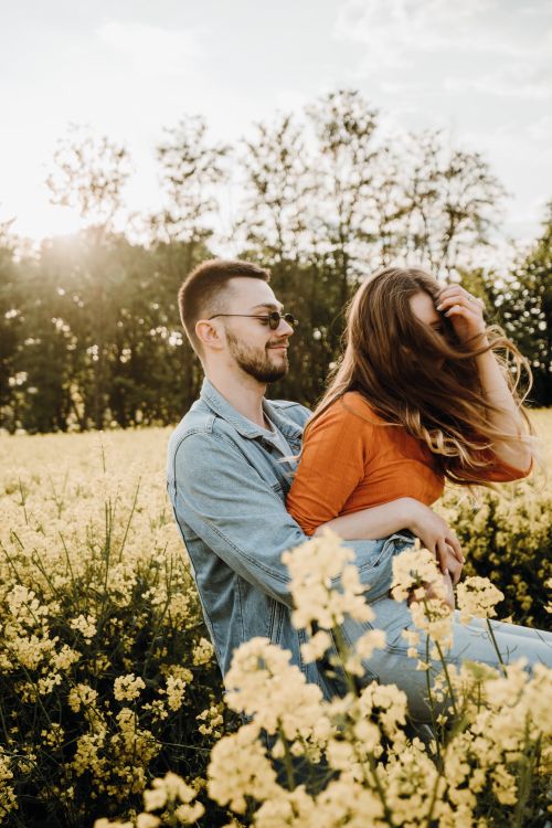 Free A happy couple embracing in a sunny flower field, creating a warm and romantic atmosphere. Stock Photo